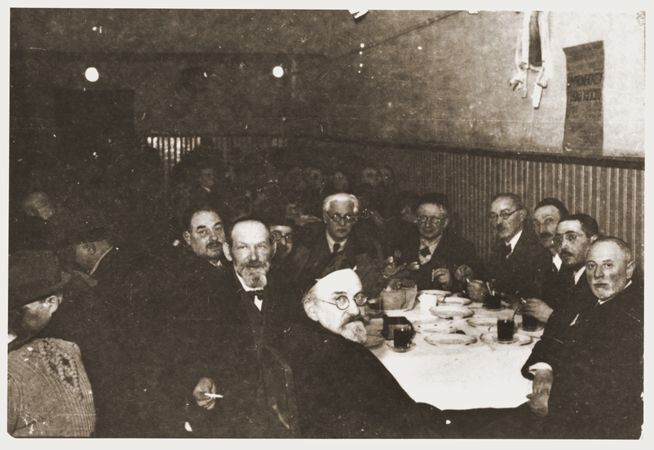 ordechai Chaim Rumkowski, chairman of the Jewish council, meets with a group of rabbis around a table in a dining hall in the Lodz ghetto